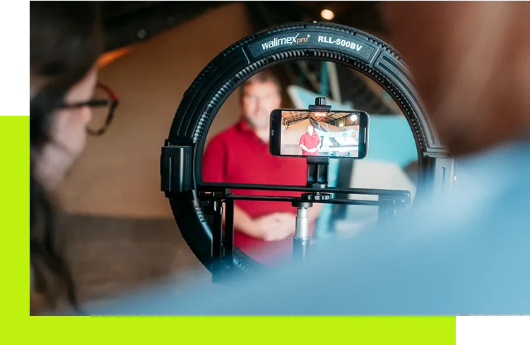 Social Advertising Werbeagentur - Videoproduktion mit Smartphone im Ringlicht, während eine Person im Hintergrund für Social-Media-Content gefilmt wird